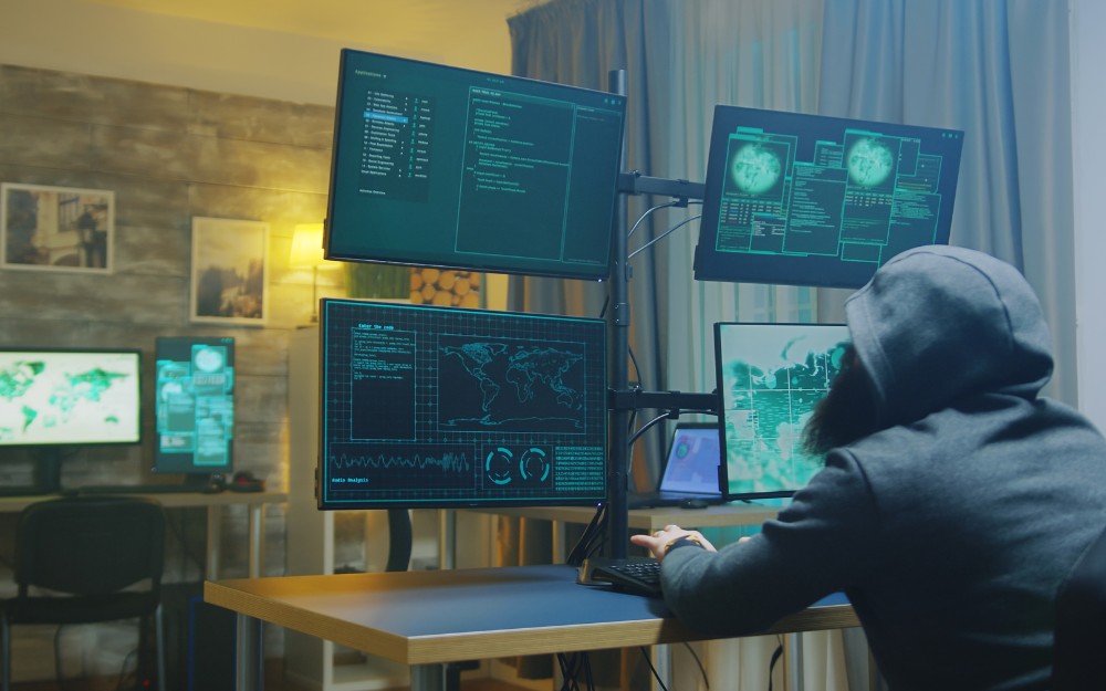 Hooded person working in front of multiple screens